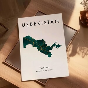 Pu&ograve; includere: Una stampa bianca con la parola "UZBEKISTAN" in nero e una mappa verde e oro dell'Uzbekistan. La stampa include anche la citt&agrave; di "Tashkent" e le coordinate. La stampa &egrave; esposta su un tavolo di legno.