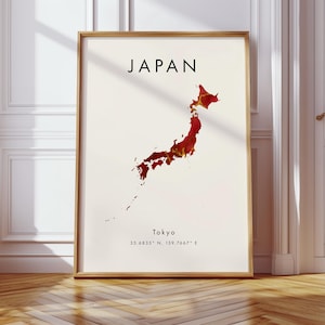 Könnte beinhalten: Ein gerahmter Druck mit einer Karte von Japan in Rot- und Goldtönen auf cremefarbenem Hintergrund. Das Wort "JAPAN" ist oben in Schwarz gedruckt, darunter "Tokyo" und Koordinaten. Der Rahmen ist hellbraun.