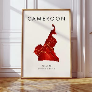 May include: Framed art print featuring a map of Cameroon in shades of red and gold, with the country's name in black at the top. The city of Yaoundé and coordinates are printed at the bottom. The print is in a wooden frame.