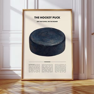 Könnte beinhalten: Gerahmter Druck mit einem dunkelblauen Hockeypuck und dem Text "THE HOCKEY PUCK" und "OFF THE FLOOR, ON THE BOARD". Der Druck hat einen beigefarbenen Hintergrund und einen Holzrahmen. Am unteren Rand des Drucks befindet sich zusätzlicher Text.