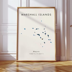 Puede incluir: Una impresión enmarcada con un mapa de las Islas Marshall. Las palabras "MARSHALL ISLANDS" están en la parte superior, con la ciudad de Majuro y las coordenadas debajo. El mapa muestra formas azules y turquesas sobre un fondo crema, enmarcado en madera.
