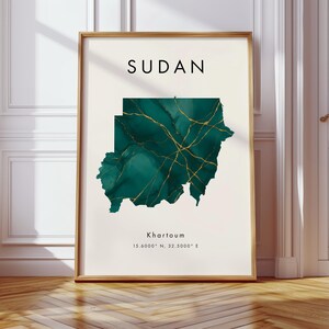 Könnte beinhalten: Gerahmter Kunstdruck mit einer Karte des Sudan in Türkis- und Goldtönen. Das Wort "SUDAN" steht oben, darunter "Khartoum" und Koordinaten. Der Rahmen ist hellbraun.
