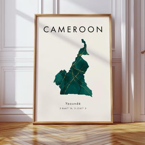 May include: Framed art print featuring the word "CAMEROON" above a teal and gold map of the country. The map is a stylized representation with gold veins. Below the map, the text reads "Yaoundé" and coordinates.