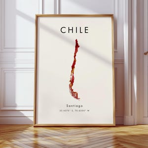 Puede incluir: Lámina enmarcada con un mapa de Chile en tonos rojos y dorados sobre un fondo crema. La palabra "CHILE" está impresa en negro en la parte superior, con "Santiago" y coordenadas debajo. El marco es de color marrón claro.