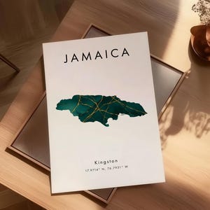 May include: A white print with the word "JAMAICA" in black, and a teal and gold map of Jamaica. The print also includes the city "Kingston" and coordinates. The print is displayed on a wooden table.