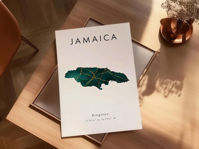 May include: A white print with the word "JAMAICA" in black, and a teal and gold map of Jamaica. The print also includes the city "Kingston" and coordinates. The print is displayed on a wooden table.
