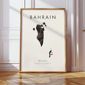 May include: A framed art print featuring a map of Bahrain. The map is black with gold accents, set against a cream background. The word "BAHRAIN" is at the top, with "Manama" and coordinates below. The frame is a light wood color.