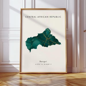 May include: Framed art print featuring a map of the Central African Republic in shades of teal and gold. The country's outline is filled with a watercolor effect, accented by gold veins. The city of Bangui and its coordinates are listed below the map.