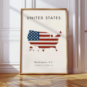 Może przedstawiać: Oprawiony wydruk przedstawiający mapę Stan&oacute;w Zjednoczonych, z nałożonym wzorem amerykańskiej flagi. Wydruk zawiera tekst "UNITED STATES" na g&oacute;rze oraz "Washington, D.C." ze wsp&oacute;łrzędnymi na dole. Rama jest w kolorze jasnobrązowym.