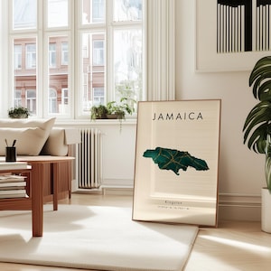May include: A framed print displaying the word "JAMAICA" above a green and gold map of Jamaica. The print is in a light-filled room with a white rug and wooden furniture. The print also includes the city of Kingston and its coordinates.