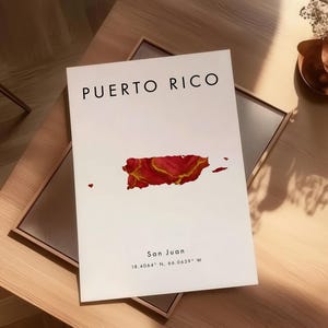 May include: A white print with the words "PUERTO RICO" in black, and a red and gold map of Puerto Rico. The print also includes the text "San Juan" and coordinates. The print is displayed on a wooden table.