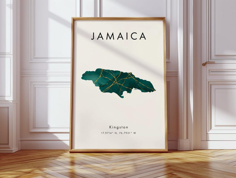 May include: A framed art print with the word "JAMAICA" at the top. Below is a teal and gold map of Jamaica. The city "Kingston" and coordinates are printed below the map. The frame is a light brown colour.