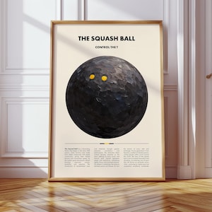 May include: Framed art print showing a textured black squash ball with two yellow dots. The text at the top reads "THE SQUASH BALL CONTROL THE T". The print is in a wooden frame and is displayed on a light beige background.