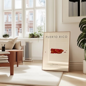 May include: A framed print with the words "PUERTO RICO" and a red and gold map of the island. Below the map are the words "San Juan" and coordinates. The print is in a bright, modern living room.