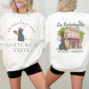May include: White sweatshirt with a cartoon rat chef holding a wooden spoon. The front design includes the text "ANYONE CAN COOK" and "GUSTEAU'S PARIS FRANCE". The back design says "La Ratatouille PARIS, FRANCE".