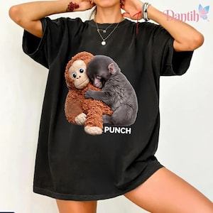 May include: Black t-shirt with a graphic of a brown toy monkey embracing a grey toy animal. The word "PUNCH" is printed in white below the image. The shirt has a relaxed, oversized fit.
