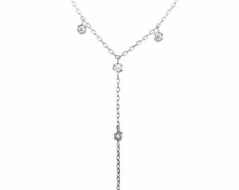 May include: A delicate silver necklace with a Y-shaped design. The necklace features multiple small, sparkling gemstones set in a bezel setting. The gemstones are evenly spaced along the chain, creating a subtle yet elegant look. The necklace is likely made of sterling silver.