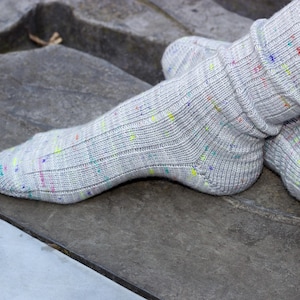 Könnte beinhalten: Nahaufnahme von grauen Stricksocken mit bunten Flecken. Die Socken sind gerippt und scheinen handgefertigt zu sein. Die Socken liegen auf einer grauen Oberfläche.