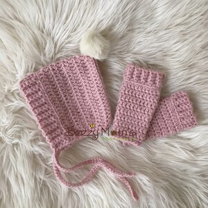 May include: A pink crocheted baby hat with a white pom pom and matching pink crocheted mittens. The hat has ties to tie under the chin.