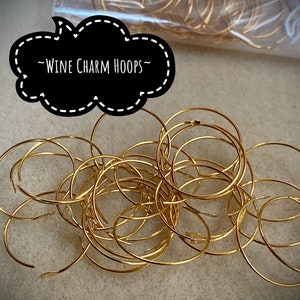 Op de afbeelding: Een stapel gouden metalen hoepels, met het label "Wine Charm Hoops".