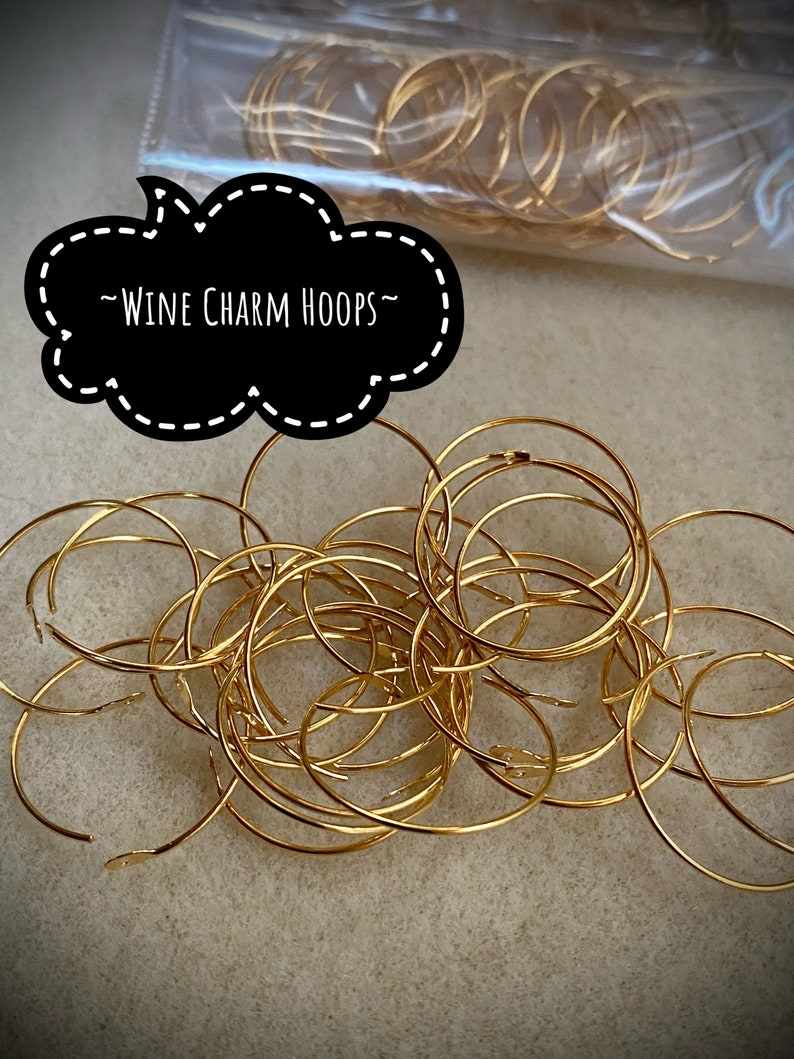 Op de afbeelding: Een stapel gouden metalen hoepels, met het label "Wine Charm Hoops".