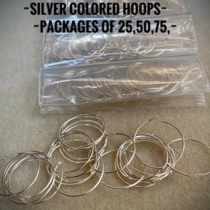 Op de afbeelding: Zilverkleurige metalen hoepels in doorzichtige plastic verpakking. De verpakking heeft de tekst "~MAKING GLASS CHARMS?~ ~SILVER COLORED HOOPS~ ~PACKAGES OF 25,50,75,~" erop gedrukt.