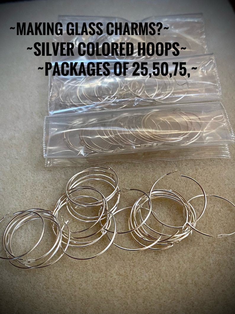 Op de afbeelding: Zilverkleurige metalen hoepels in doorzichtige plastic verpakking. De verpakking heeft de tekst "~MAKING GLASS CHARMS?~ ~SILVER COLORED HOOPS~ ~PACKAGES OF 25,50,75,~" erop gedrukt.