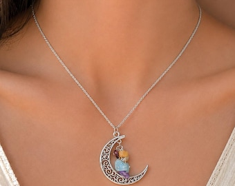 May include: A silver-toned necklace featuring a crescent moon pendant with intricate filigree cutouts. The pendant is adorned with a cluster of small, raw, multi-colored gemstone chips in shades of light blue, yellow, purple, and dark red.