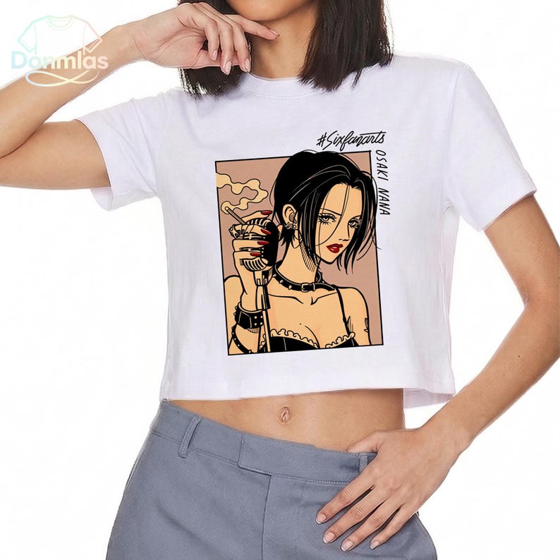 Puede incluir: Top corto blanco con una ilustraci&oacute;n de estilo manga de una mujer con cabello negro, labios rojos y un cigarrillo. El gr&aacute;fico est&aacute; enmarcado en un cuadro marr&oacute;n claro, con el texto "#Sixfanarts" y "OSAKI NANA" impreso en la camiseta.