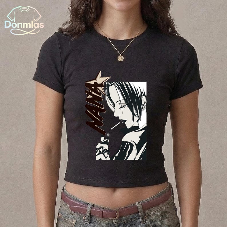 May include: Black crop top with a manga-style illustration of a character smoking, with the word "NANA" in a bold font. The graphic is in black and white. The top has a crew neck and short sleeves.