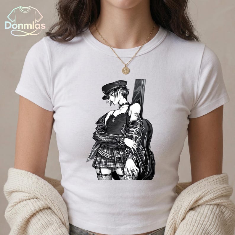 May include: White t-shirt featuring a black and white anime-style illustration of a person with a guitar. The person is wearing a black hat, jacket, and plaid skirt. The shirt has the text "Donmlas" in the upper left corner.