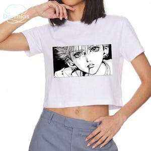 May include: White crop top featuring a black and white manga-style graphic. The graphic depicts a person with multiple piercings and a chain. The shirt has short sleeves and a crew neck.