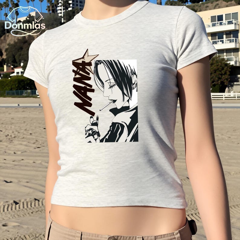 May include: A pale grey t-shirt with a black and white illustration of a woman smoking. The word "NANA" is printed vertically beside the image, with a star above the first letter.