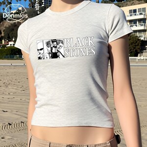May include: A light gray t-shirt featuring a black and white graphic of four stylized faces and the words "BLACK STONES" in bold, white letters. The shirt is short-sleeved and has a crew neck.