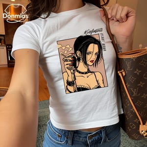Puede incluir: Camiseta blanca con un gr&aacute;fico de una mujer de pelo negro, sosteniendo un micr&oacute;fono y un cigarrillo. El gr&aacute;fico incluye el texto "OSAKI NANA" y "#Sixfanarts". La camiseta se combina con unos vaqueros azules.