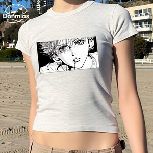May include: A light gray t-shirt featuring a black and white manga-style graphic of a person with multiple piercings and a chain. The graphic is rectangular and centered on the shirt.