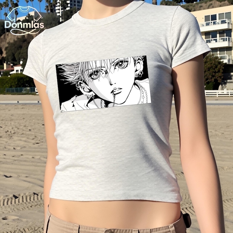 May include: A light gray t-shirt featuring a black and white manga-style graphic of a person with multiple piercings and a chain. The graphic is rectangular and centered on the shirt.