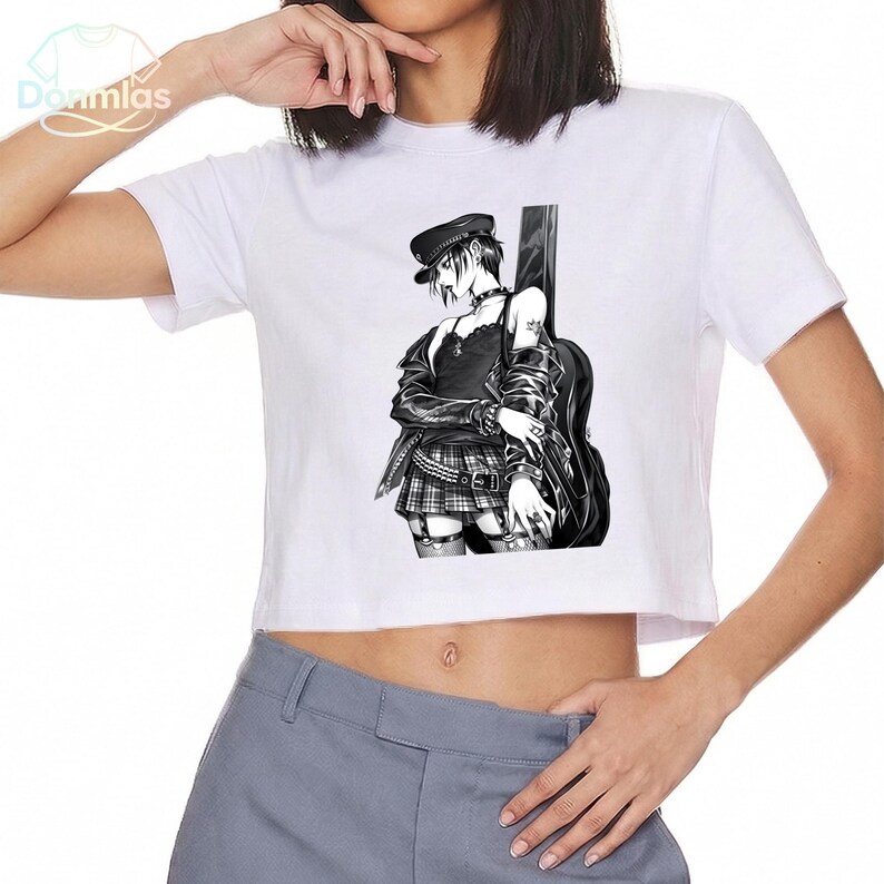 May include: White crop top featuring a black and white anime-style illustration of a person with a guitar case. The illustration depicts a person wearing a hat, jacket, and plaid skirt. The top has the brand name "Donmlas" printed on the upper left.
