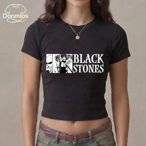 May include: Black crew neck t-shirt with a graphic of stylized faces and the text "BLACK STONES" in white. The shirt is a cropped style and is made of a dark fabric.
