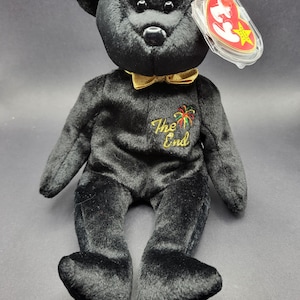 Può includere: Orso di peluche nero Beanie Baby con un papillon dorato e il testo "The End" con un'immagine di fuochi d'artificio ricamata sul petto. L'orso ha un'etichetta a stella rossa con il logo Ty.
