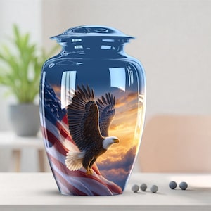 May include: A blue cremation urn with a patriotic design. The urn features an American flag and a soaring bald eagle against a sunset sky. The urn is a vase shape with a lid.