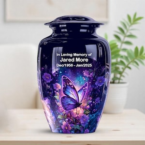 May include: A navy blue cremation urn with a butterfly and floral design. The urn has a glossy finish and features the text "In Loving Memory of Jared More Dec/1956 - Jan/2025". The butterfly is purple and blue.