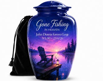May include: A deep blue cremation urn featuring a sunset lake scene with a wooden dock, a chair, a fishing rod, and a lantern. The text reads "Gone Fishing IN HEAVEN John Dennis forever Love 9/1/80 ~ 23/6/26". A black velvet drawstring bag sits behind the urn.