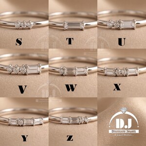 May include: Nine silver rings, each with a different design of small, clear gemstones. The rings are presented against a neutral backdrop. The letters S, T, U, V, W, X, Y, and Z are displayed on the rings. The Dhanlaxmi Jewels logo is in the bottom right.