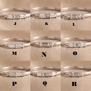 May include: Nine silver rings, each with a different design of baguette and round-cut gemstones. The rings are presented on a neutral backdrop, each labelled with a letter from J to R.