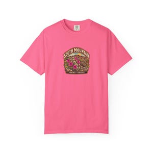 May include: A bright pink short-sleeve t-shirt featuring a central graphic of a desert landscape with blooming pink cacti. The text reads South Mountain and Phoenix Arizona in a curved brown banner above and below the illustration.