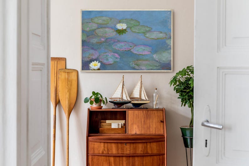 May include: A framed painting of water lilies in a pond hangs above a wooden cabinet. Two decorative sailboat models and a small potted plant sit on top of the cabinet. Two wooden oars lean against the wall.