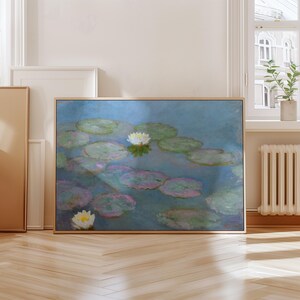 May include: A framed art print of a water lily pond. The painting features lily pads in shades of green and pink, with white water lilies. The background is a soft blue, and the frame is a light wood color.
