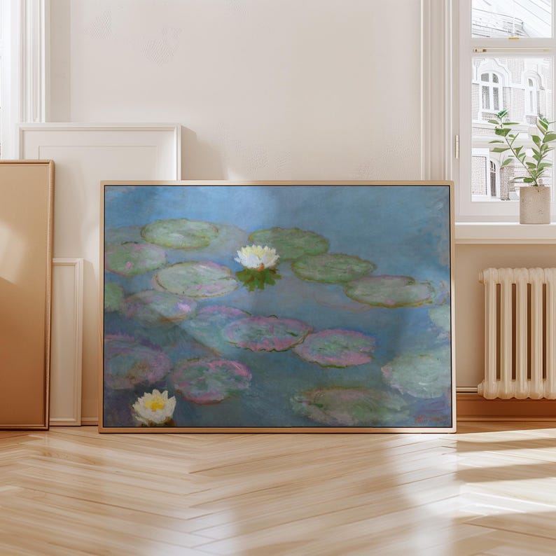 May include: A framed art print of a water lily pond. The painting features lily pads in shades of green and pink, with white water lilies. The background is a soft blue, and the frame is a light wood color.