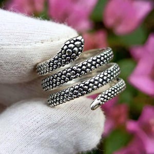May include: A silver-toned metal ring shaped like a coiled snake. The band features a textured, raised scale pattern across its entire surface, wrapping around the finger in a spiral design with a defined head at one end and a tapered tail at the other.
